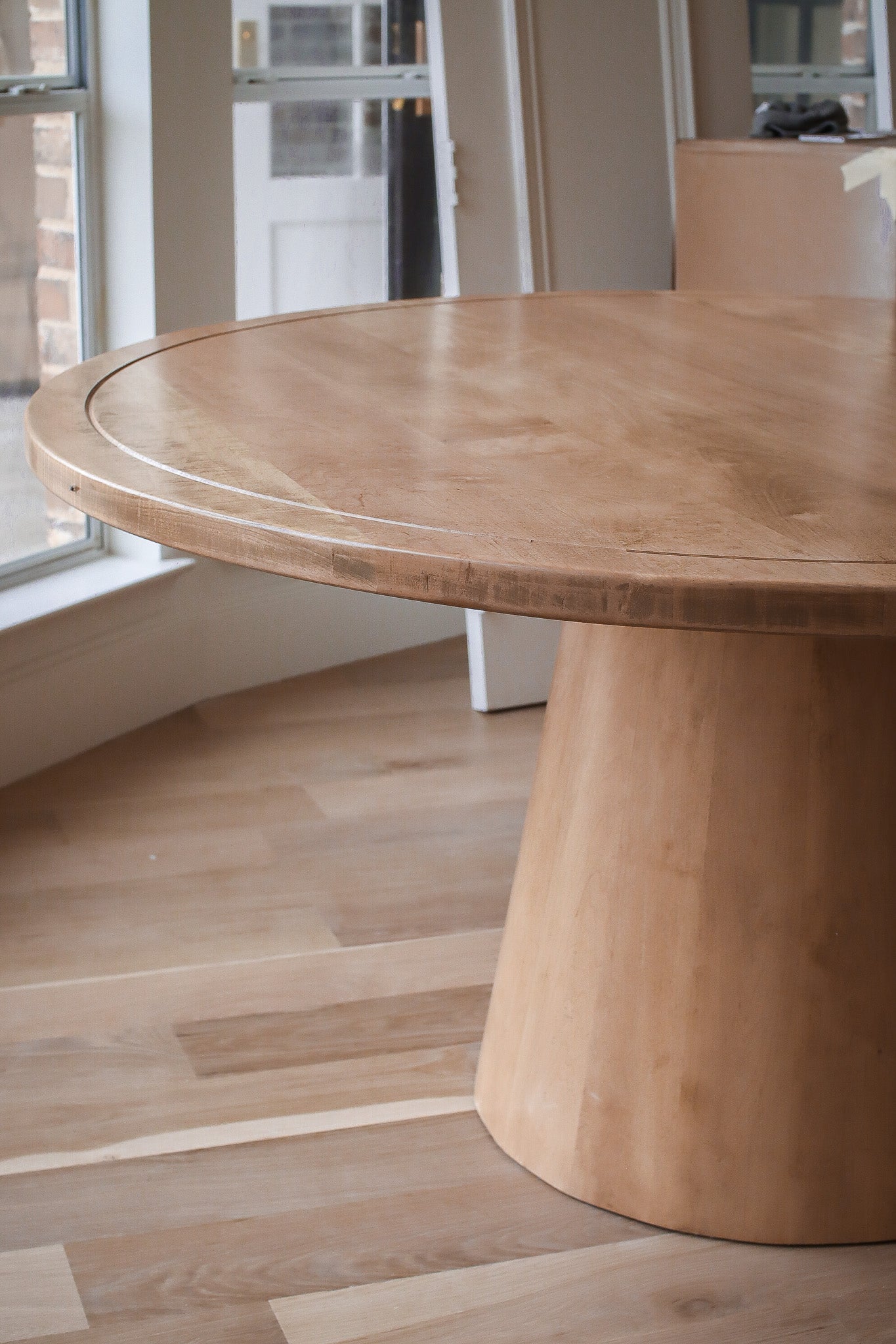 A round solid wood dining table positioned in a large texas modern dining room. The table showcases its natural grains, grooves, and the beautiful golden oak color.