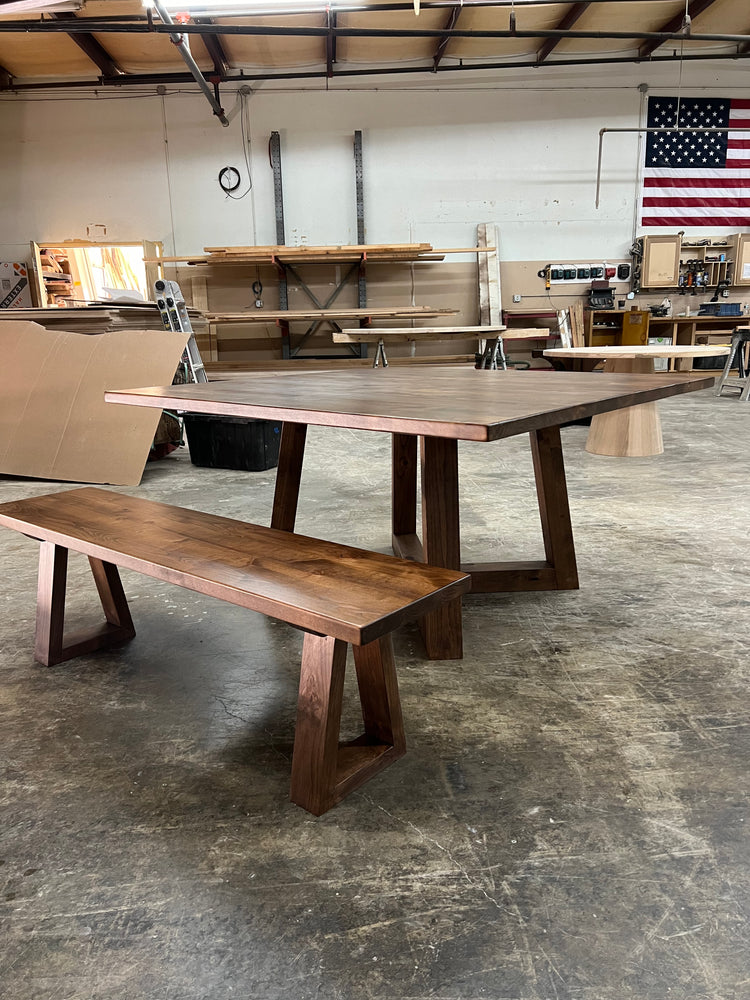shown is a large dark brown square dining table in a woodworking shop
