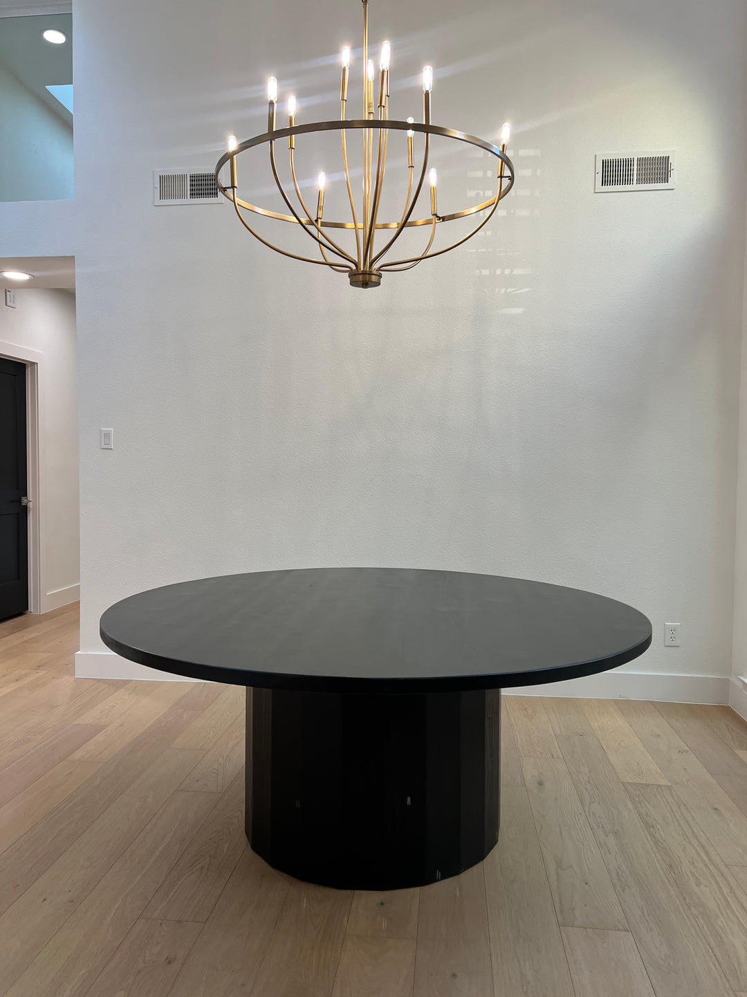 Large Black round dining table in a modern Texas home under a round chandelier