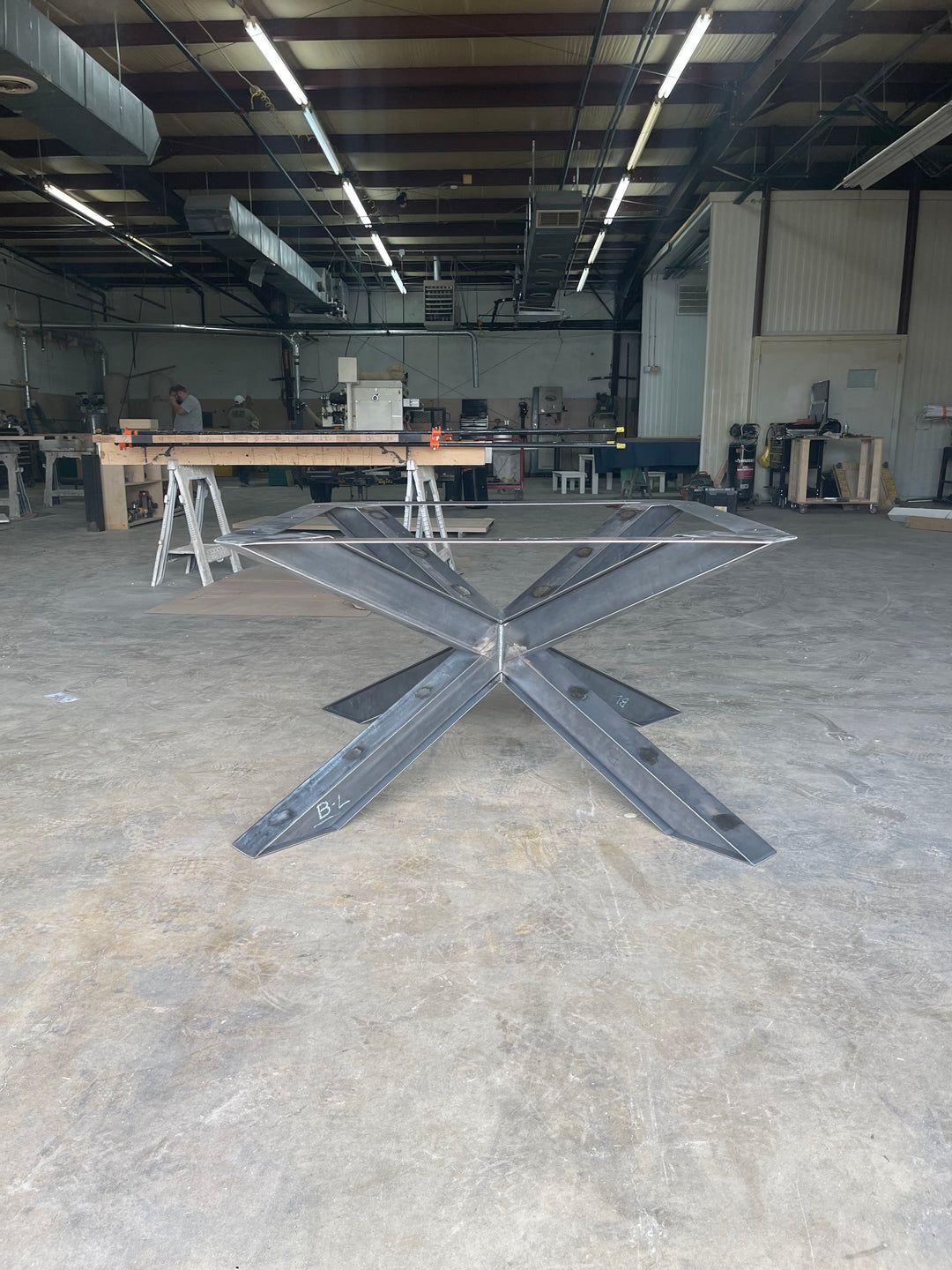 ished metal spider base in a woodworking shop, displaying raw metalwork and the detailed structure, surrounded by tools and wood material