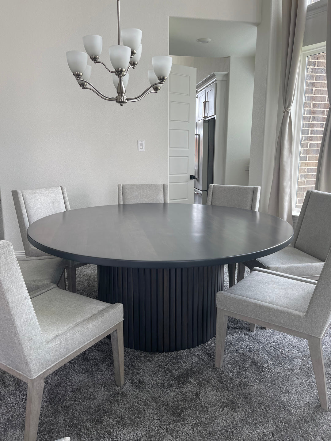 72-inch fluted round dining table surrounded by seven large gray upholstered chairs, creating an elegant and inviting dining space