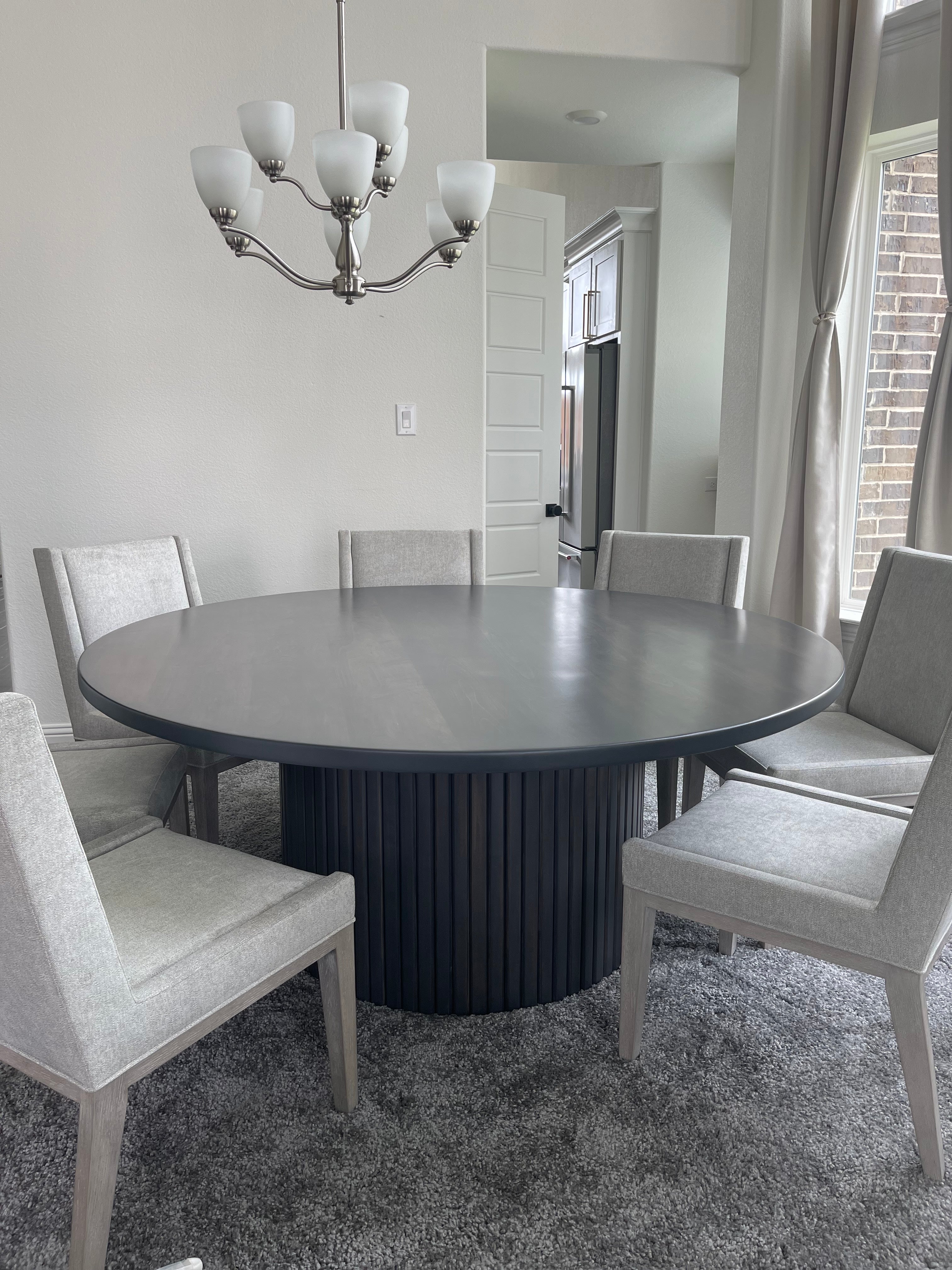 72-inch fluted round dining table surrounded by seven large gray upholstered chairs, creating an elegant and inviting dining space