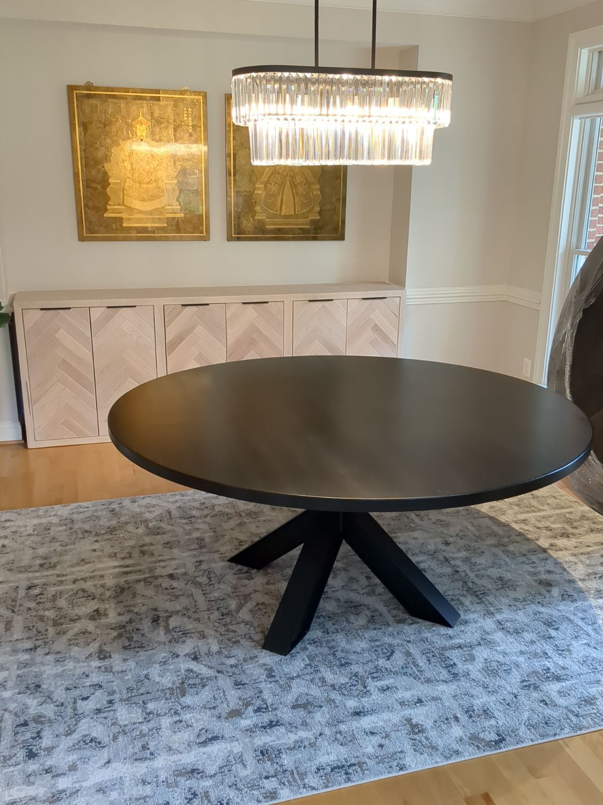Black round table on a metal base, placed on a modern blue rug, with a herringbone buffet table positioned behind it, adding a stylish and contemporary touch to the room