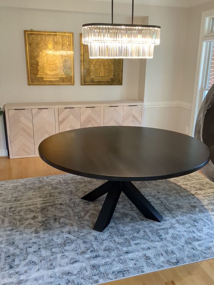 Black round table on a metal base, placed on a modern blue rug, with a herringbone buffet table positioned behind it, adding a stylish and contemporary touch to the room