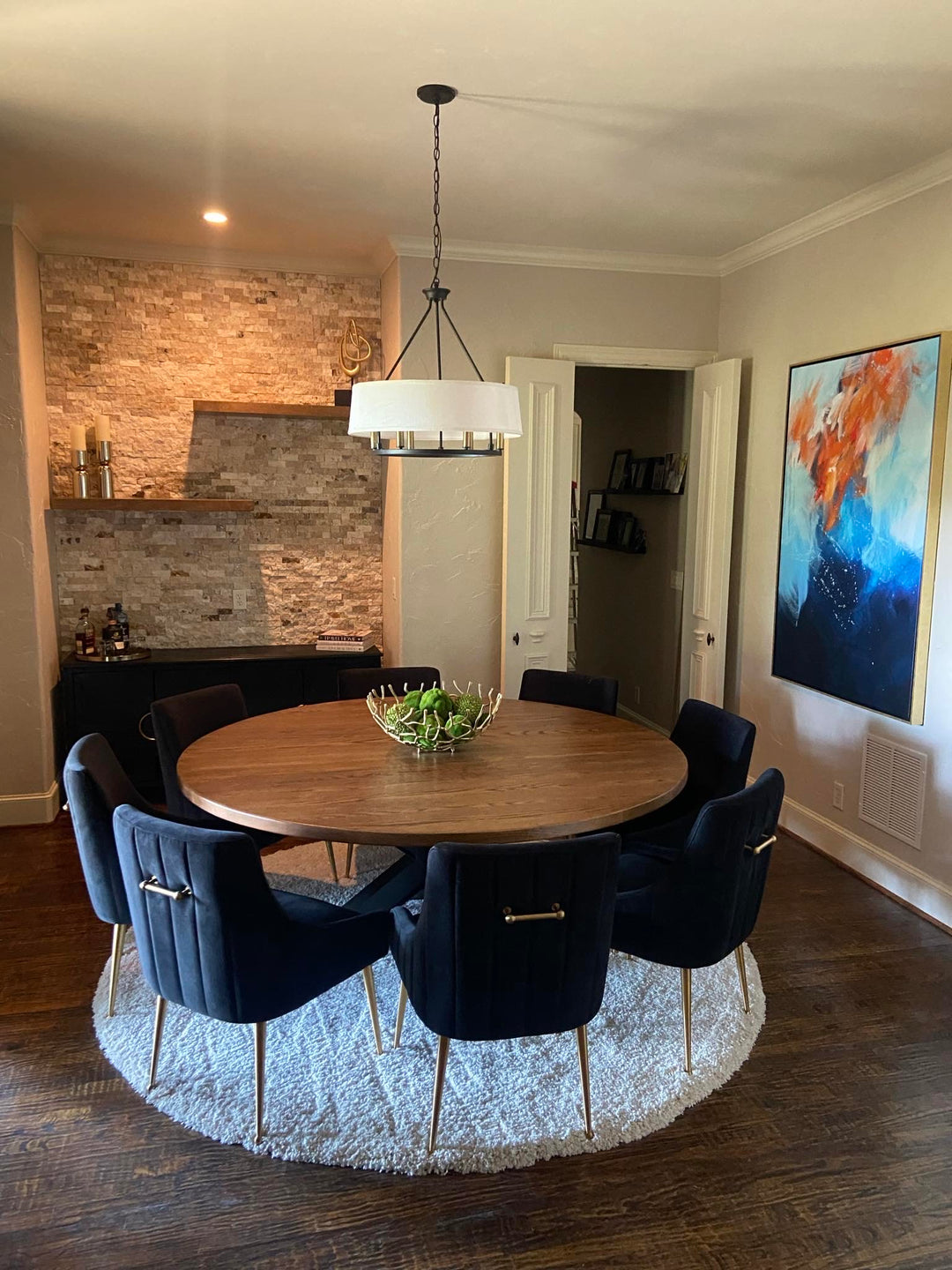 Orange pal table surrounded by eight large, wide blue upholstered chairs, set in a modern rustic dining room with a blend of warm and contemporary elements