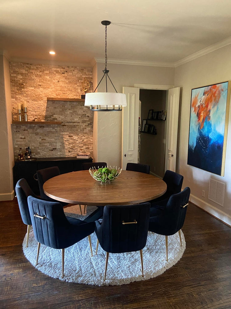 Orange pal table surrounded by eight large, wide blue upholstered chairs, set in a modern rustic dining room with a blend of warm and contemporary elements