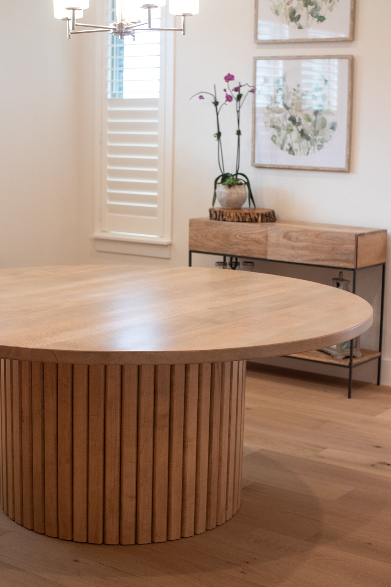 Large handcrafted fluted base of a dining table, with a beautiful entry table in the background, creating an elegant and inviting atmosphere