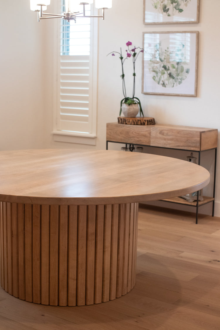 Large handcrafted fluted base of a dining table, with a beautiful entry table in the background, creating an elegant and inviting atmosphere