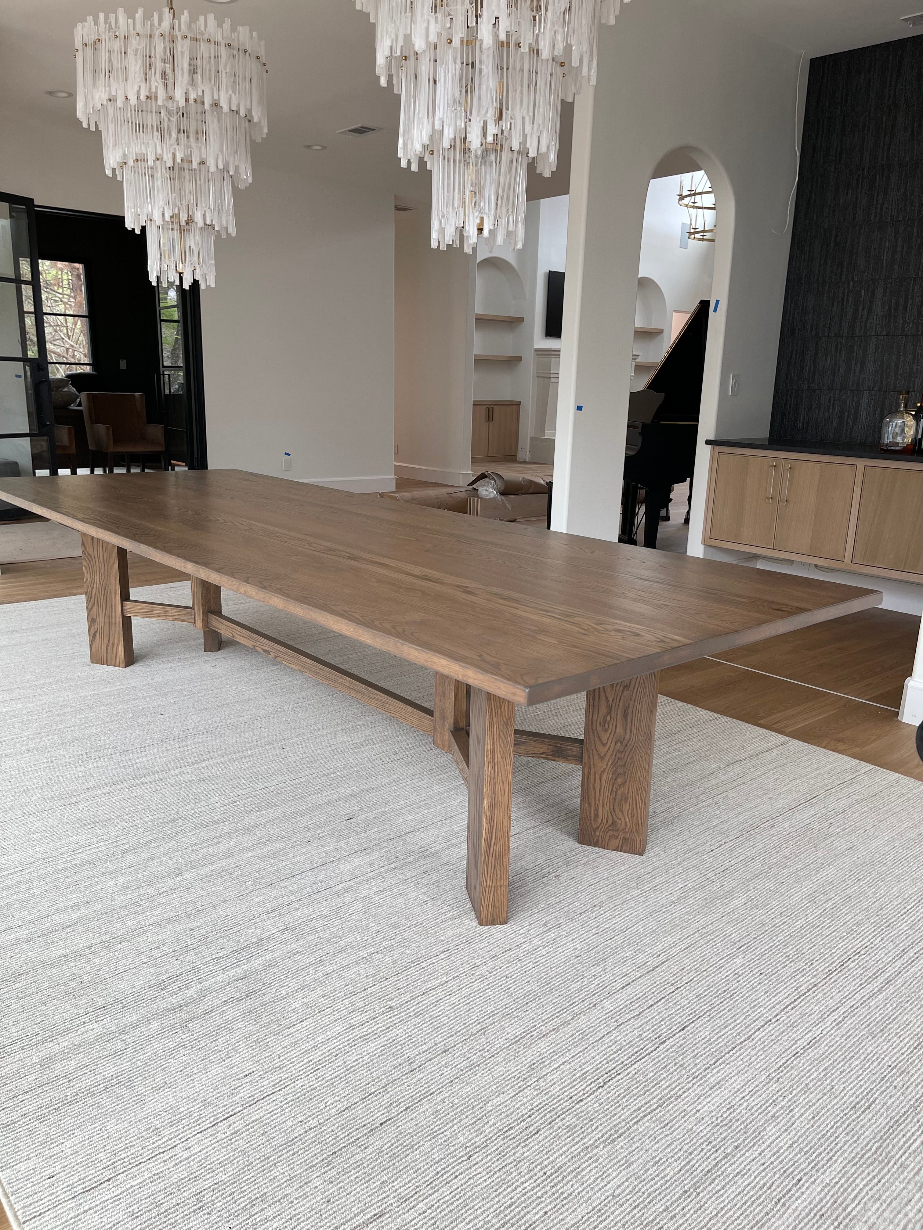 Large rectangular Briarsmoke white oak dining table in a grand and modern dining room, complemented by two elegant feather-like chandeliers and a gorgeous piano in the background, creating a luxurious and sophisticated atmosphere