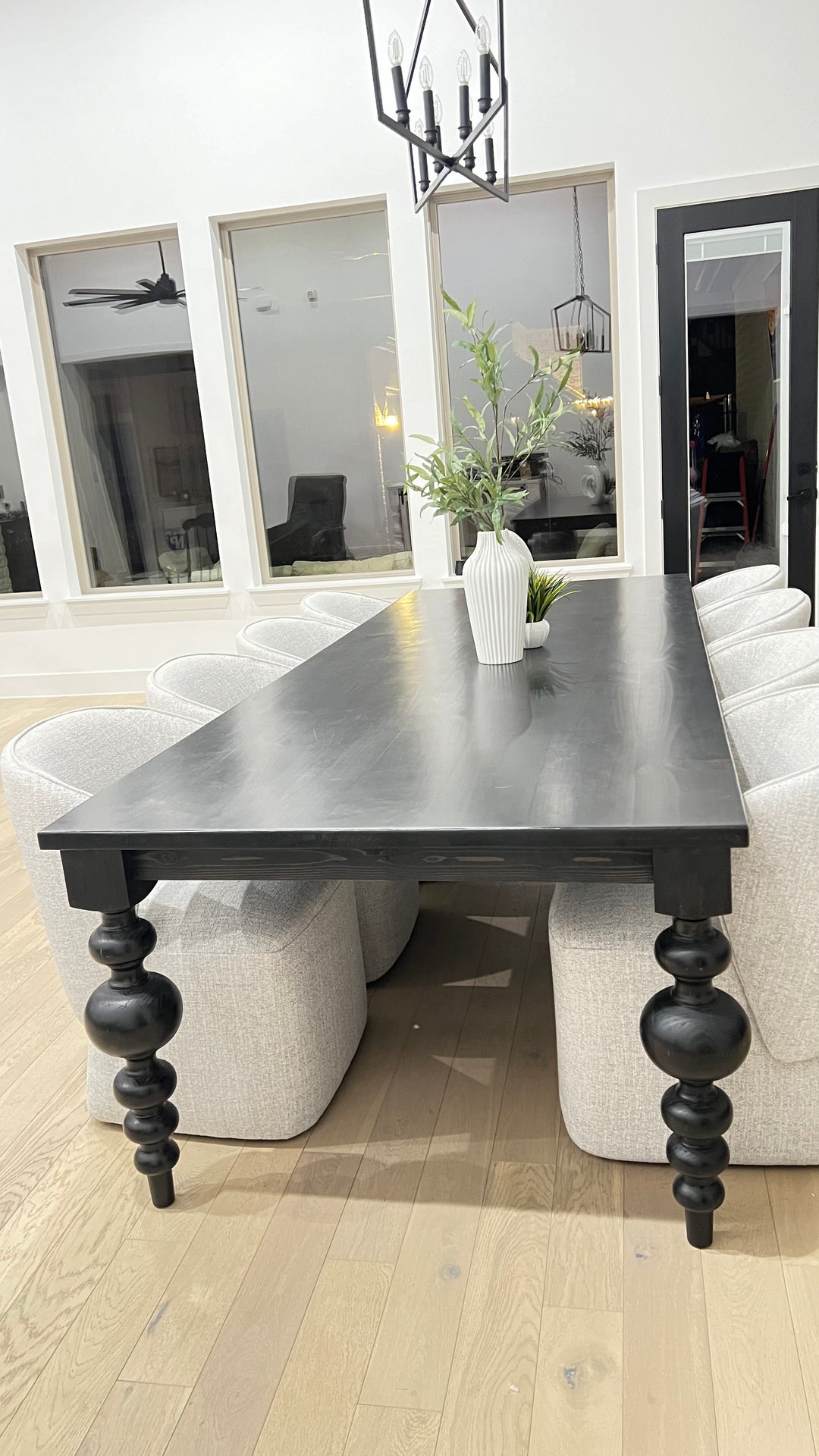 Large black rectangular table with curved pedestal legs, surrounded by eight large upholstered light gray chairs. A unique modern plant serves as the centerpiece, adding a touch of style to the space