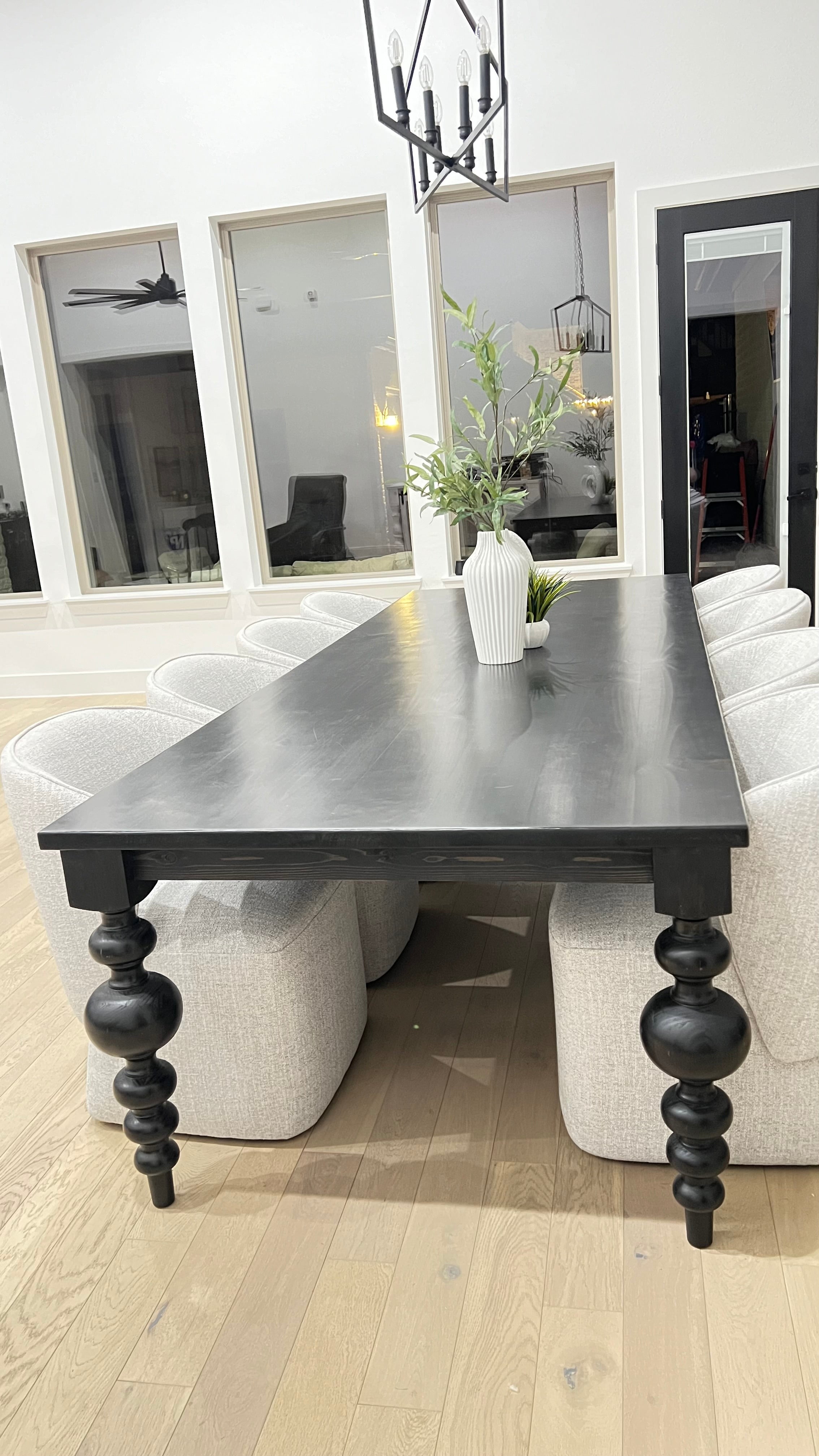 Large black rectangular table with curved pedestal legs, surrounded by eight large upholstered light gray chairs. A unique modern plant serves as the centerpiece, adding a touch of style to the space