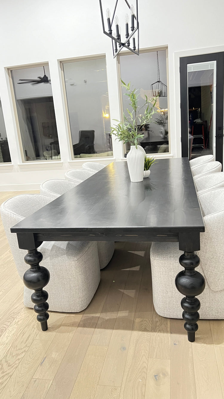 Large black rectangular table with curved pedestal legs, surrounded by eight large upholstered light gray chairs. A unique modern plant serves as the centerpiece, adding a touch of style to the space