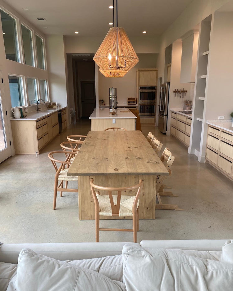 Light brown wooden rectangular dining table in a warm, cozy kitchen, surrounded by eight chairs, creating an inviting and family-friendly atmosphere