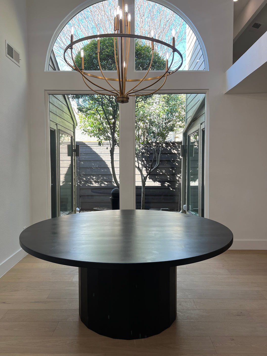 A spacious black round dining table situated in a contemporary Texas home, elegantly illuminated by a round chandelier.