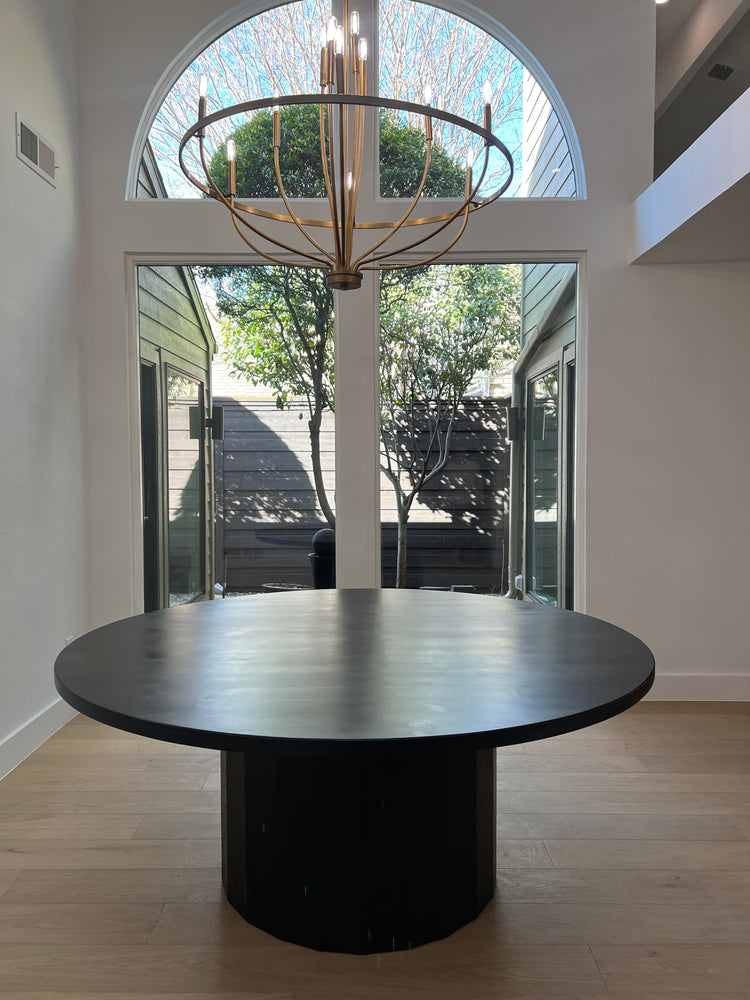 A spacious black round dining table situated in a contemporary Texas home, elegantly illuminated by a round chandelier.