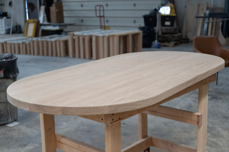 Custom white oak table in a workshop setting with various tools and materials in the background
