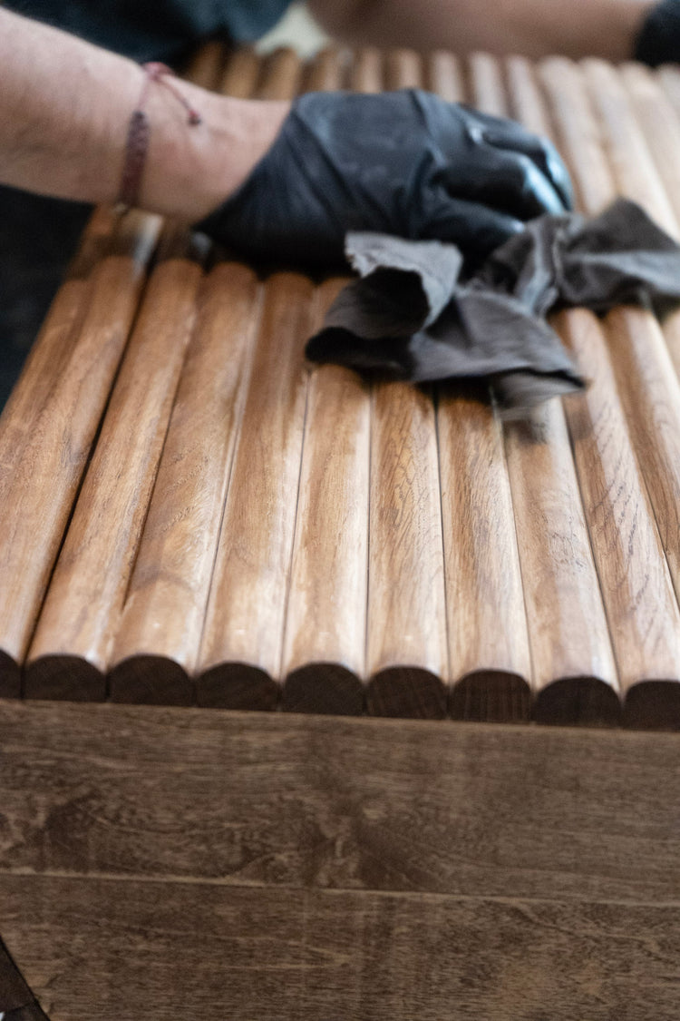 Person wearing black gloves staining a white oak flutedsurface with a cloth.