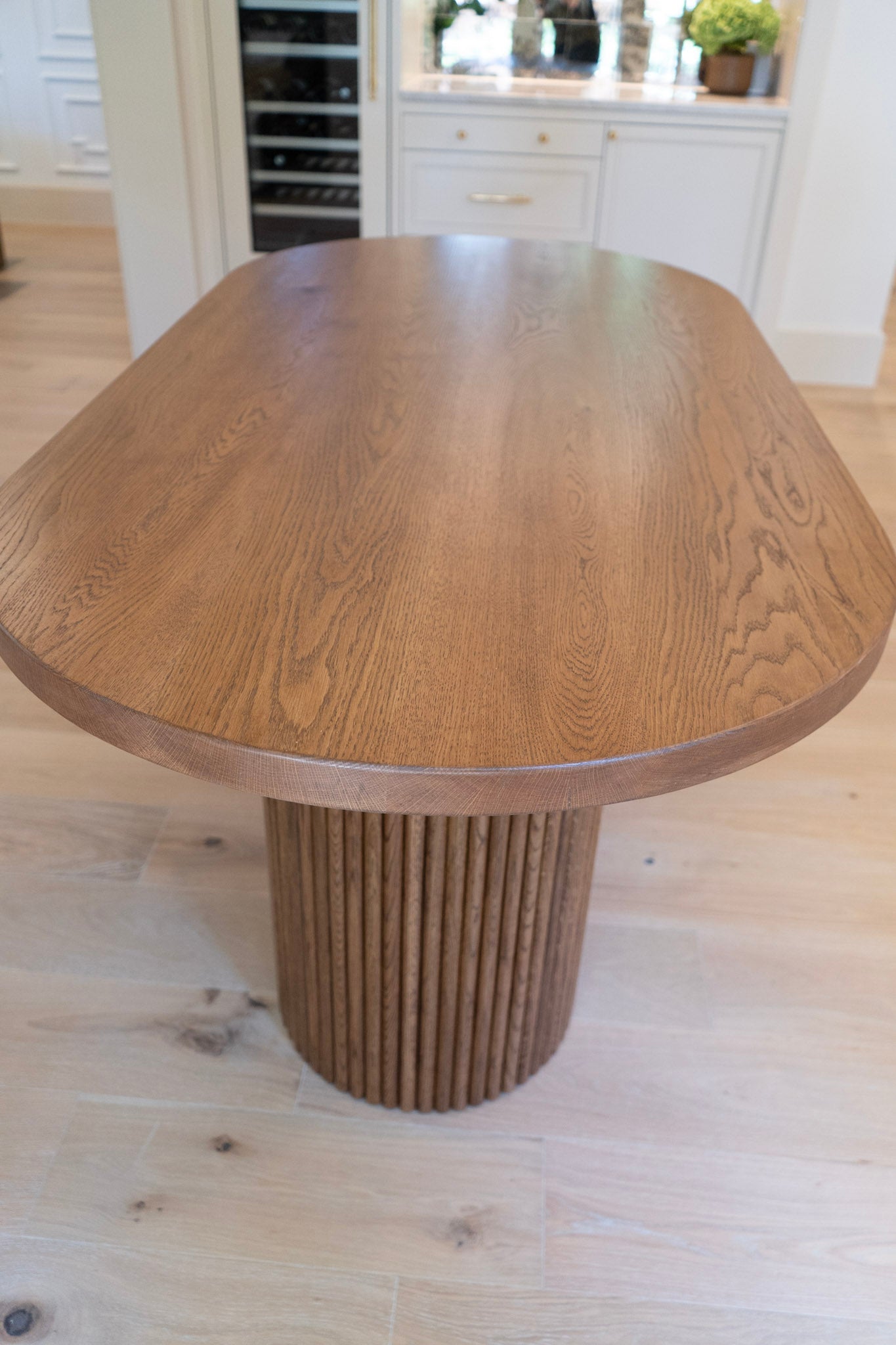 Wooden oval white oak dining table with a ribbed fluted cylindrical base in a kitchen setting