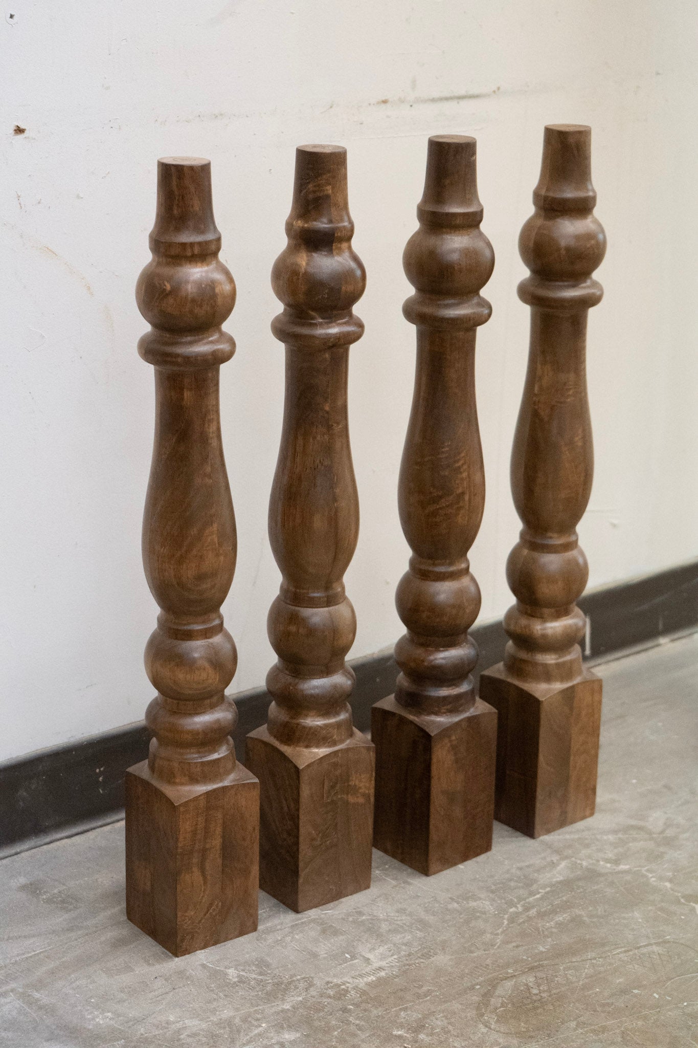 Four wooden balusters on a gray floor against a white wall.
