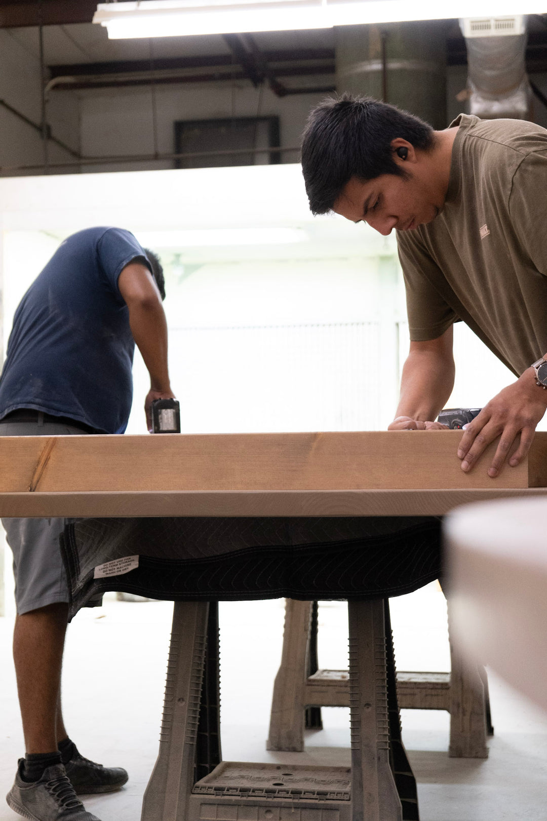 Two people working on a wooden table in a workshop setting.