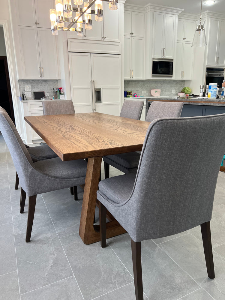 Rectangular oak dining table with a smooth, organic frame, surrounded by six wide gray upholstered chairs, creating a stylish and comfortable dining space