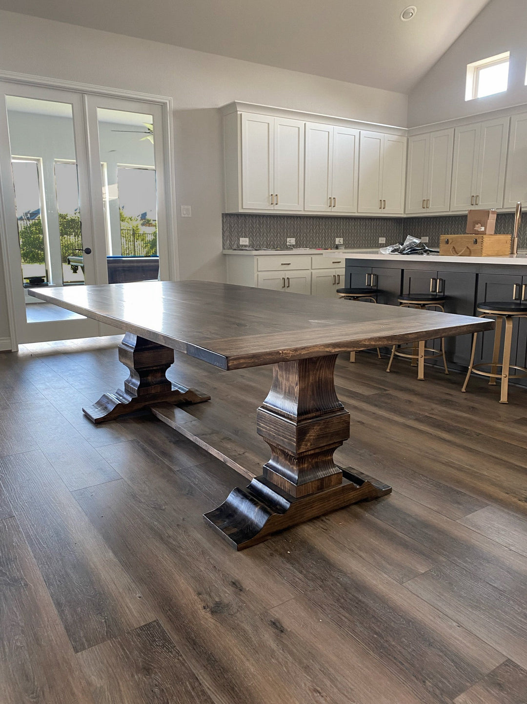 Rectangular wooden handcrafted pedestal dining table in a modern rustic kitchen, showcasing intricate craftsmanship and natural wood details that complement the warm, contemporary design