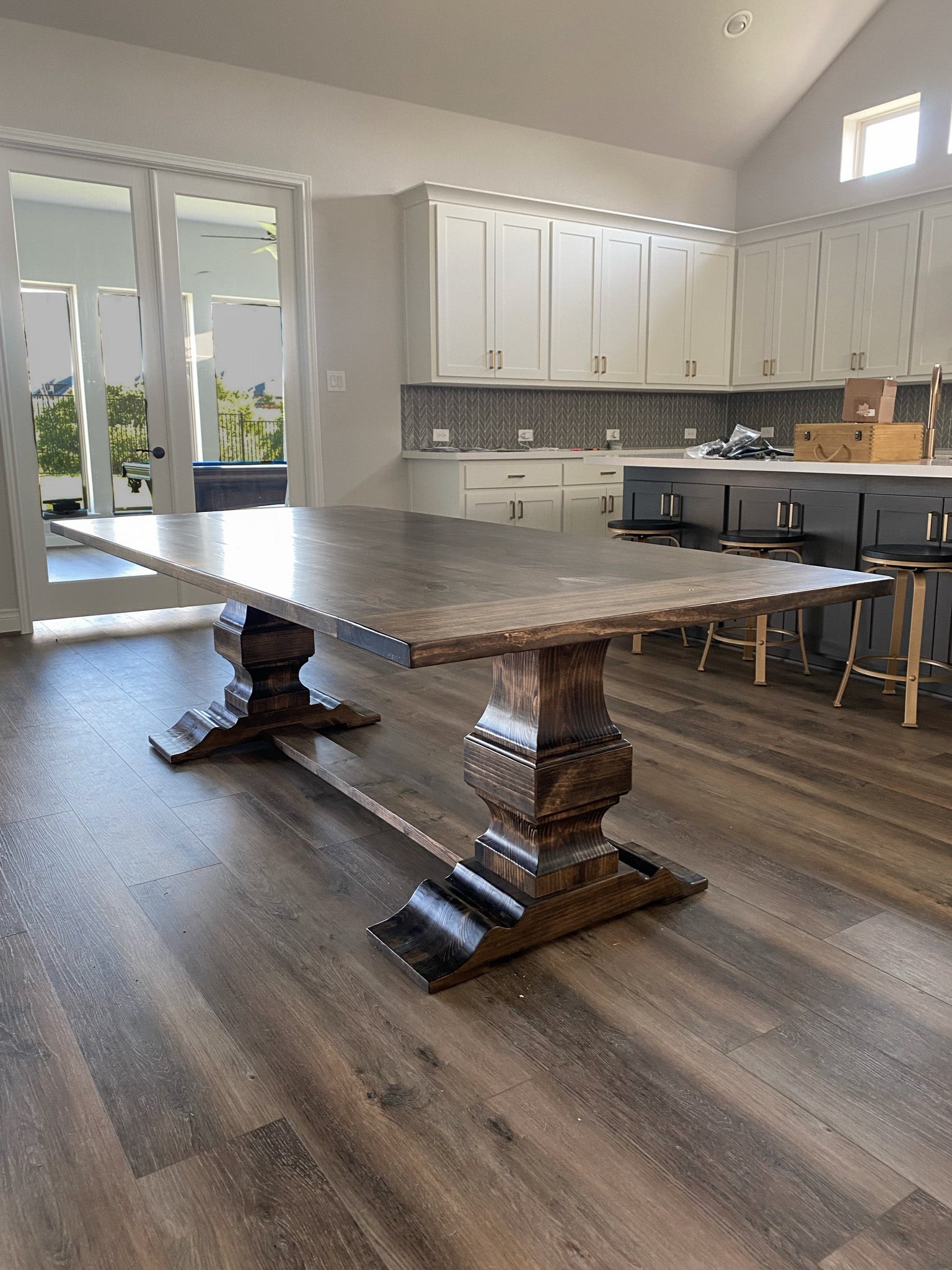 Rectangular wooden handcrafted pedestal dining table in a modern rustic kitchen, showcasing intricate craftsmanship and natural wood details that complement the warm, contemporary design
