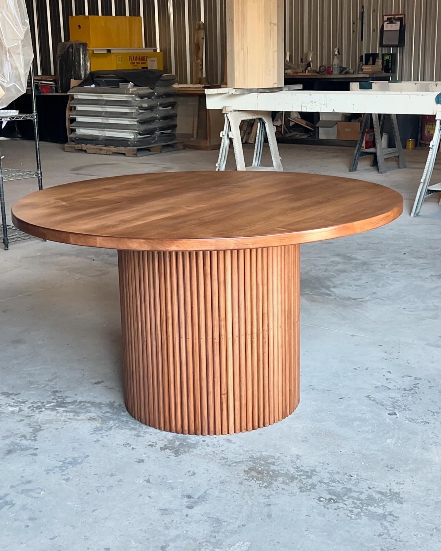 Special walnut fluted maple round dining table in a woodworking shop, showcasing its intricate craftsmanship and natural wood details against the backdrop of tools and wood materials