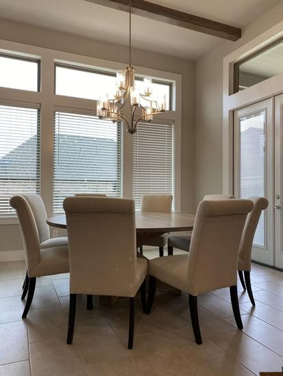 A round wooden dining table in a bright Texas dining room, featuring eight chairs. The table has a extra chunky pedestal base that adds a modern farmhouse touch.