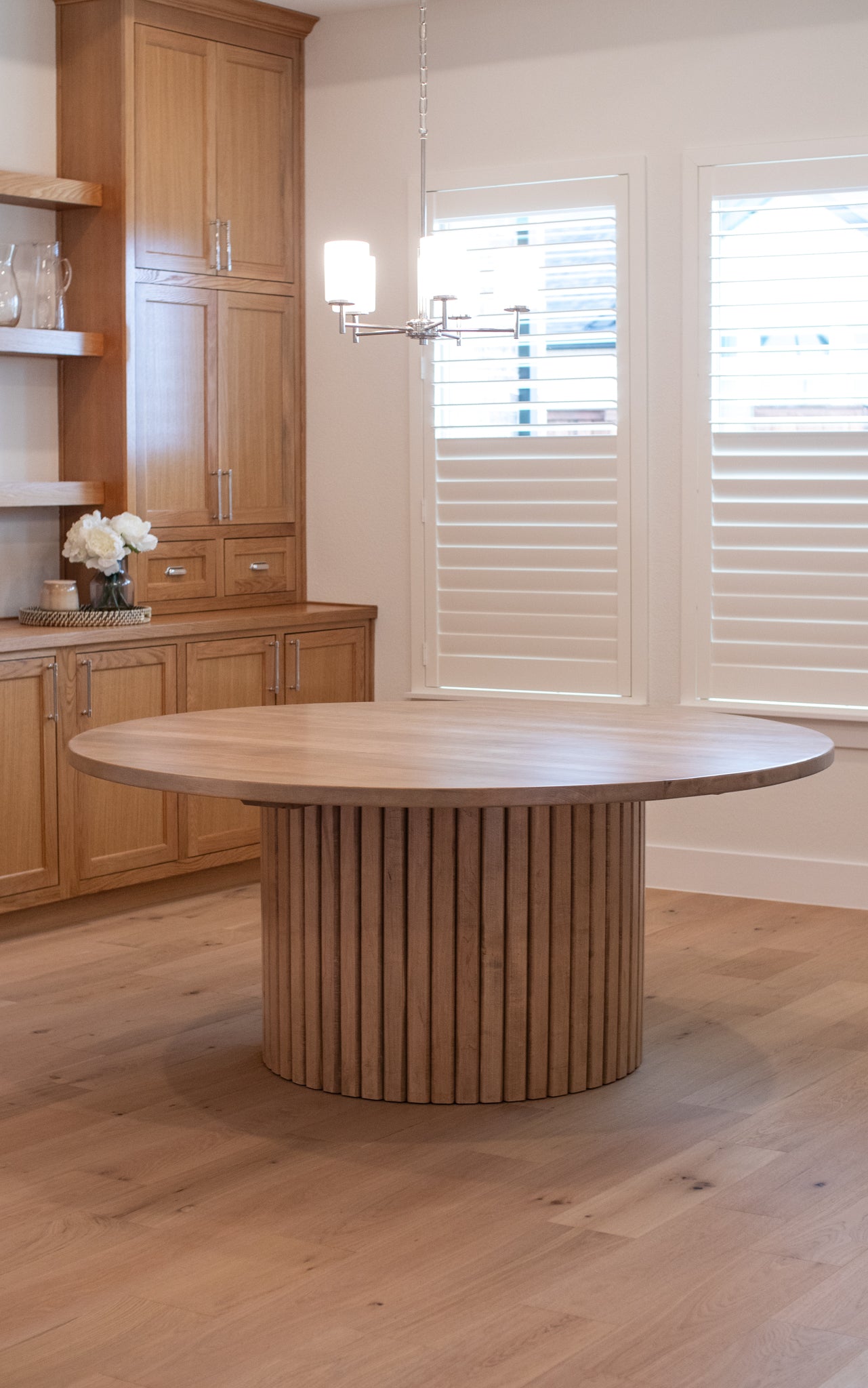 Large 72-inch fluted round dining table in a cozy, warm wooden dining room, with oak cabinets in the background and natural light streaming through the windows.