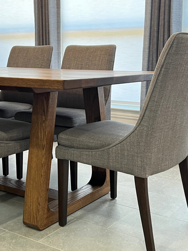 Rectangular oak dining table with a smooth, organic frame, surrounded by four wide gray upholstered chairs, creating a stylish and comfortable dining space
