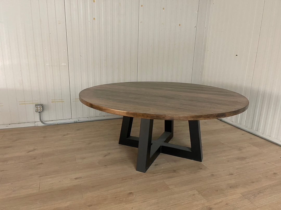 Large maple round tabletop sitting on a black metal trapezoid base, creating a striking contrast between the warm wood and sleek, modern base
