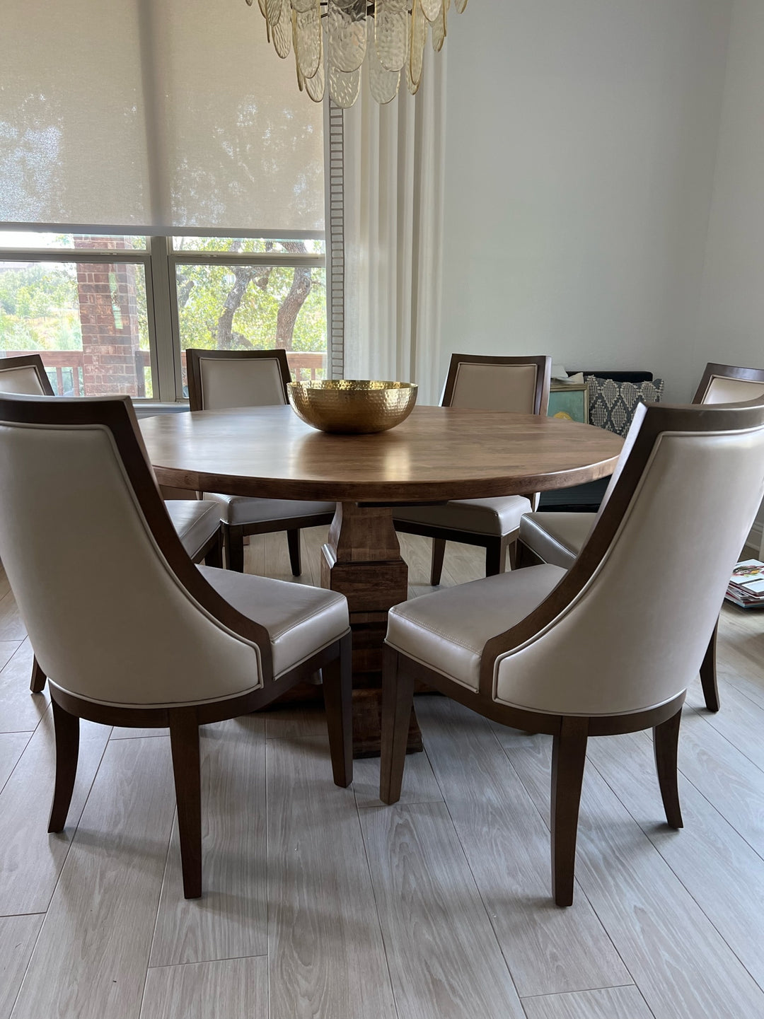 Warm brown round pedestal dining table in a modern, classy dining room, surrounded by six large cream leather chairs, creating an elegant and inviting atmosphere