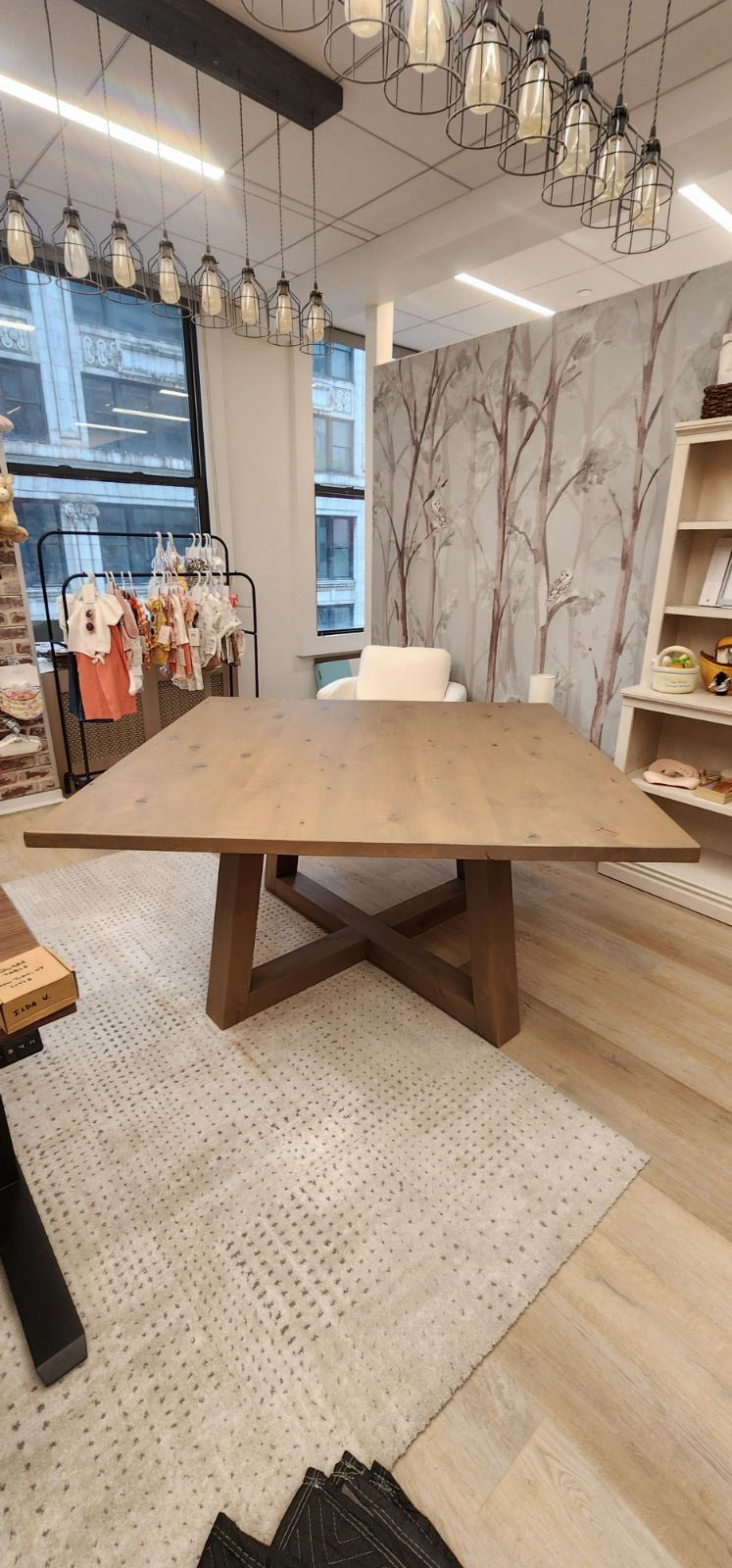 "Square children's dining table with colorful clothes, displayed in a playful kids' showroom with bright decor in the background."