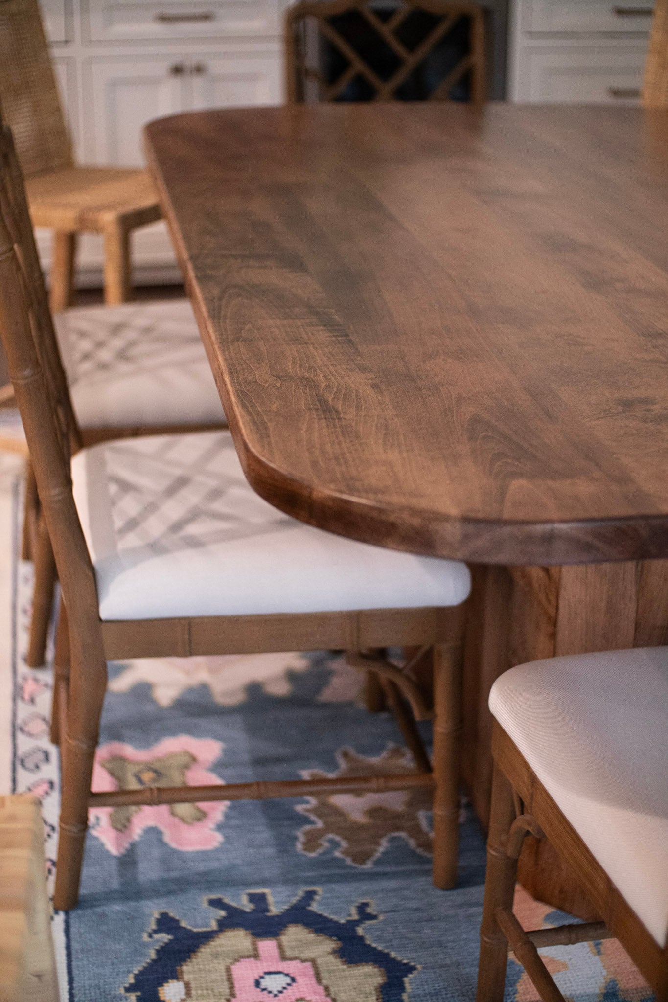rectangular table with rounded corners and an oblong cylinder base on a green/blue patterned rug with nice chairs around it
