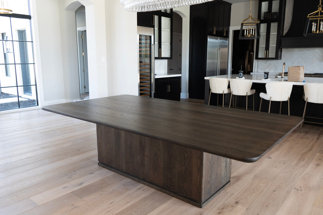 Large dark white oak dining table in a modern kitchen setting with white chairs.