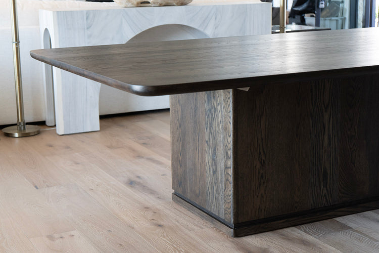 Large dark white oak dining table in a modern kitchen setting with white chairs.