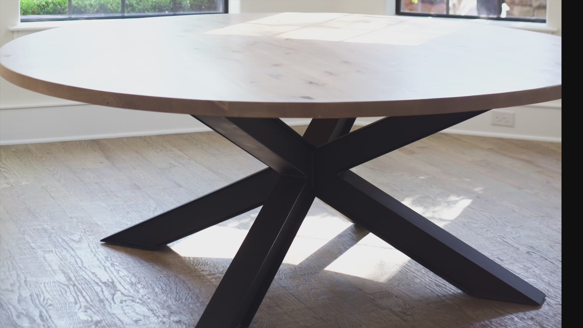 different angles of the Large modern round wooden dining table. It showcases the black metal base. The table is bathed in natural light from surrounding windows.