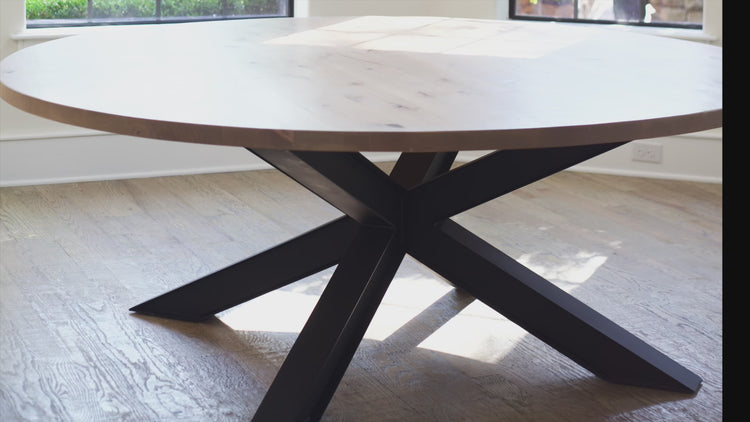 different angles of the Large modern round wooden dining table. It showcases the black metal base. The table is bathed in natural light from surrounding windows.