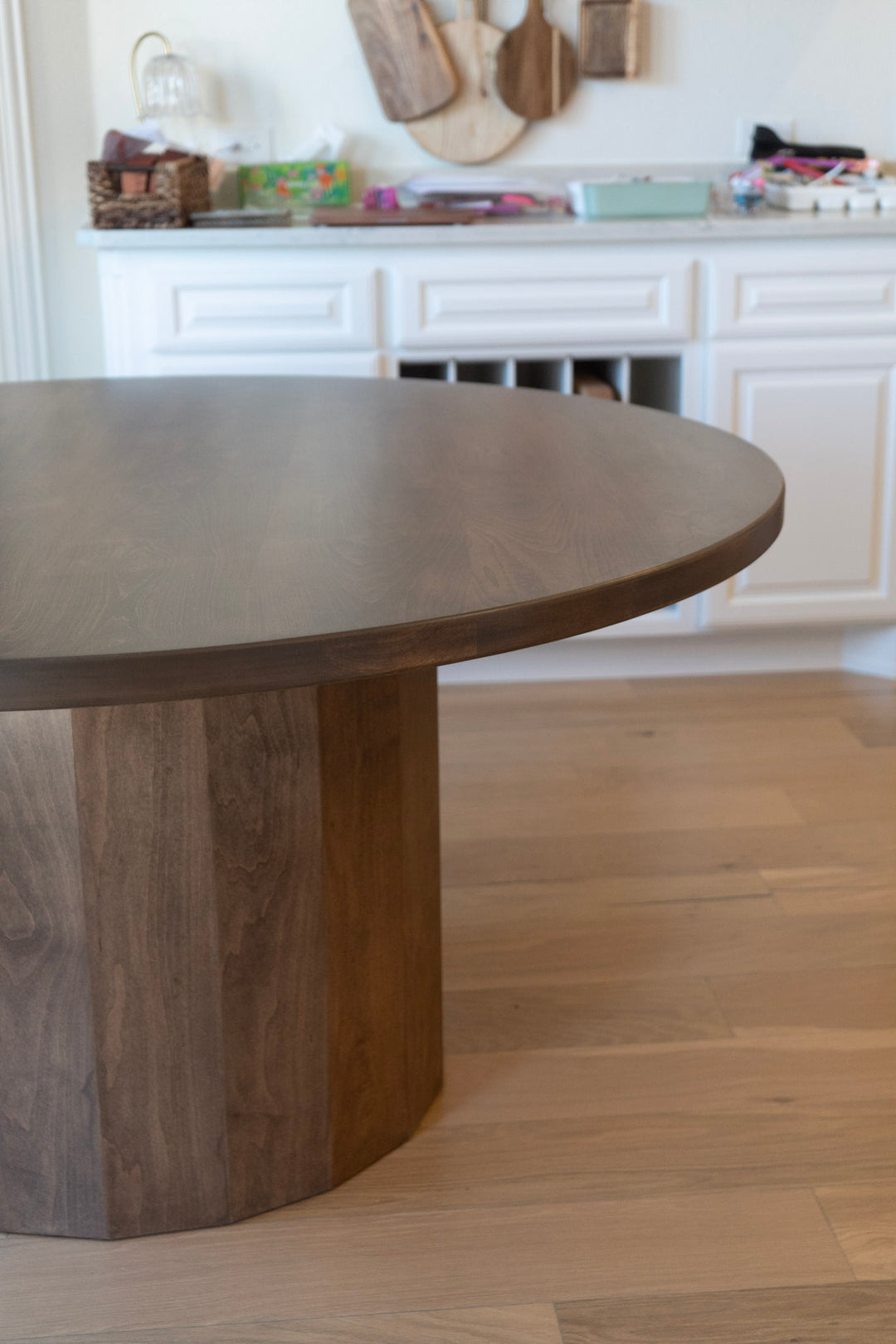 Wooden dining table in a kitchen setting with white cabinets and wooden flooring.