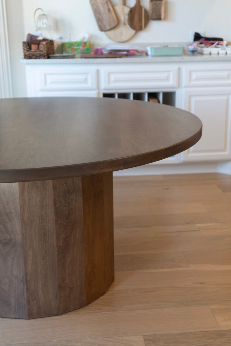 Wooden dining table in a kitchen setting with white cabinets and wooden flooring.
