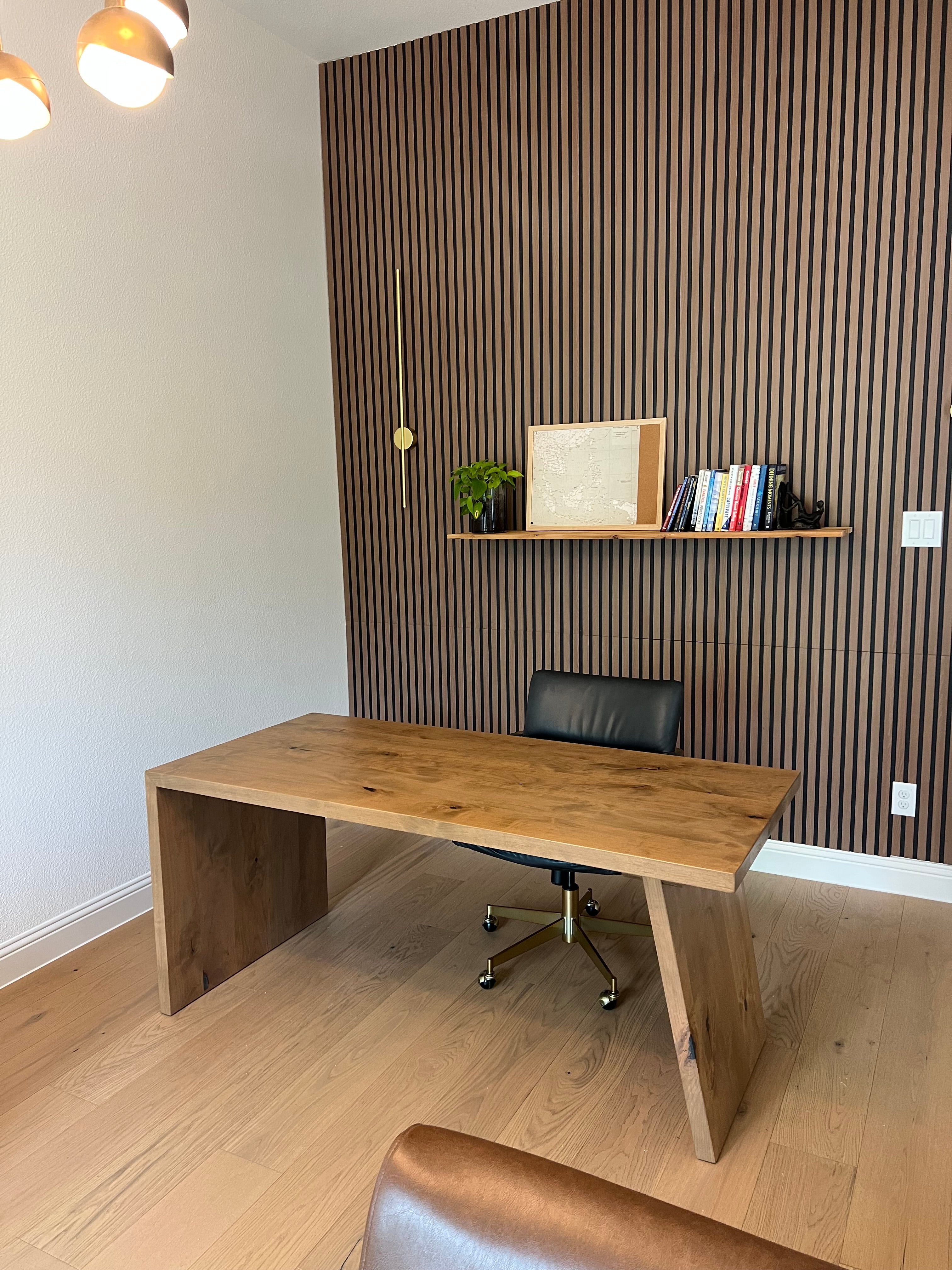 Wooden desk with chair against a slatted wall in a room with white floor and ceiling.