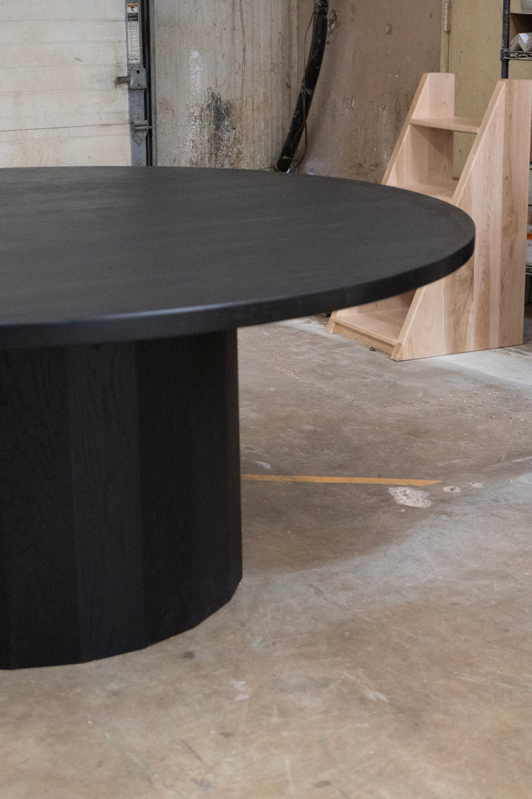 Black round table in a warehouse setting with concrete floor and wooden shelves.