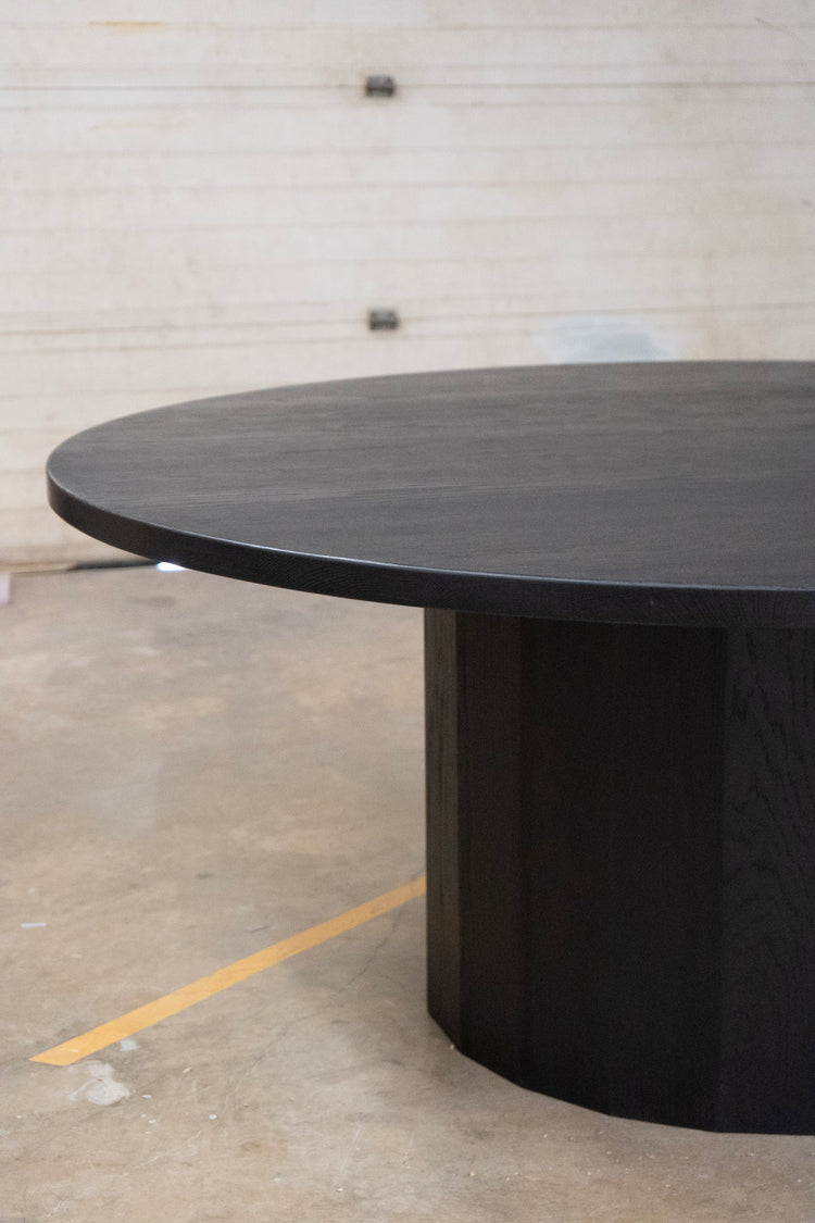 Black round table in an industrial setting with concrete floor and white wall.