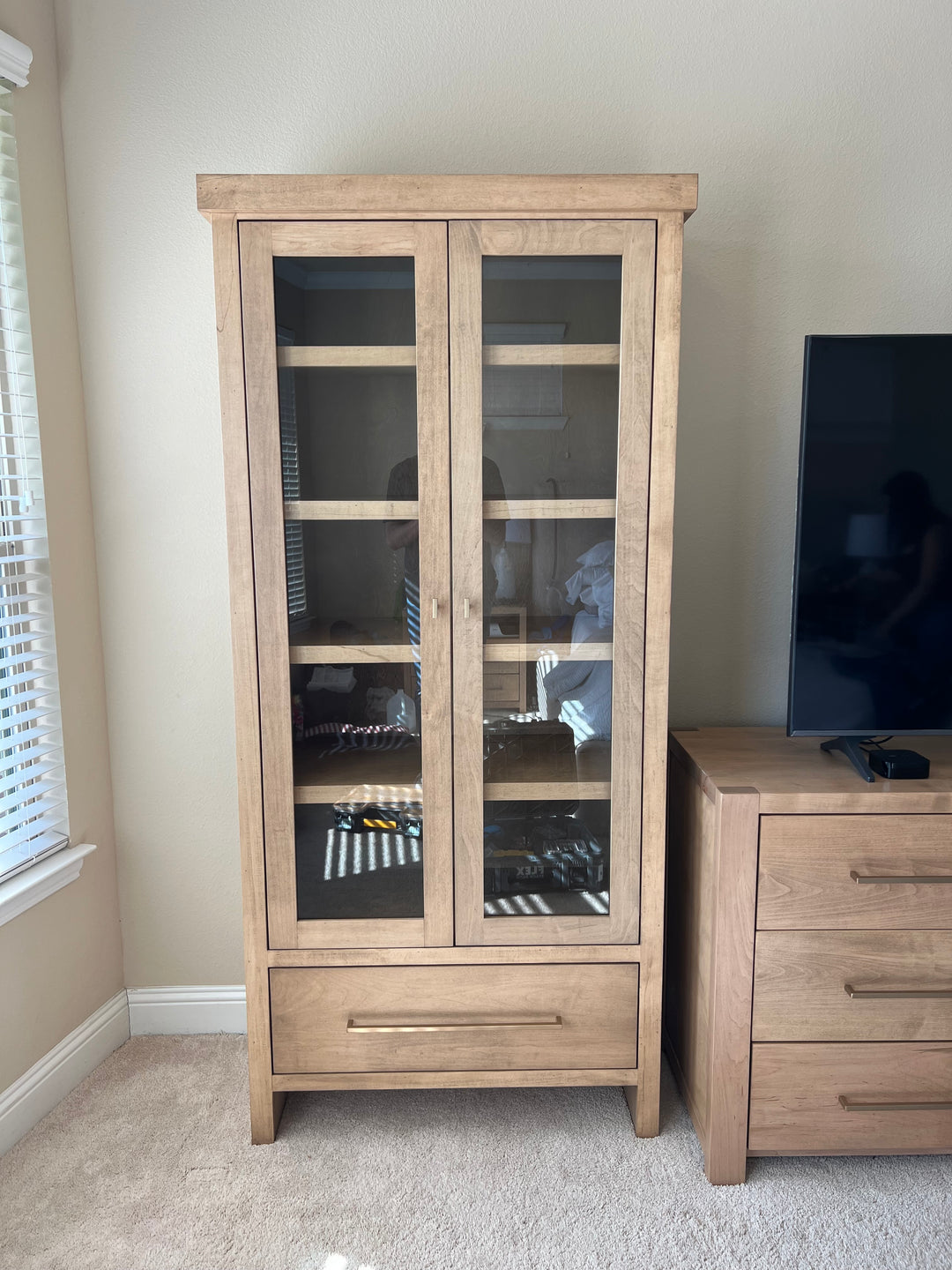 Wooden cabinet with glass doors and dresser in a bedroom.