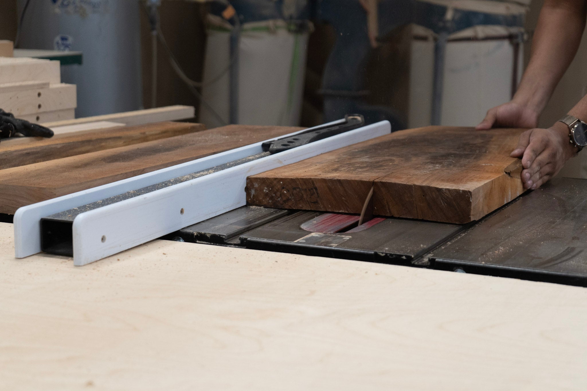 Walnut board being cut on a table saw with a person's hand visible.