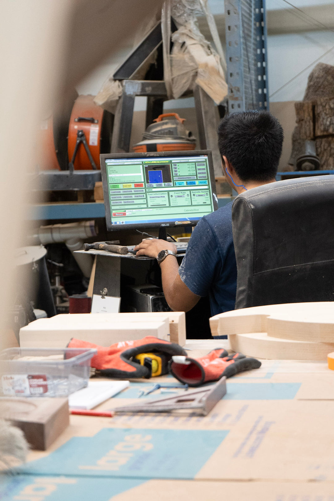 Person using a laptop in a workshop setting with tools and equipment around