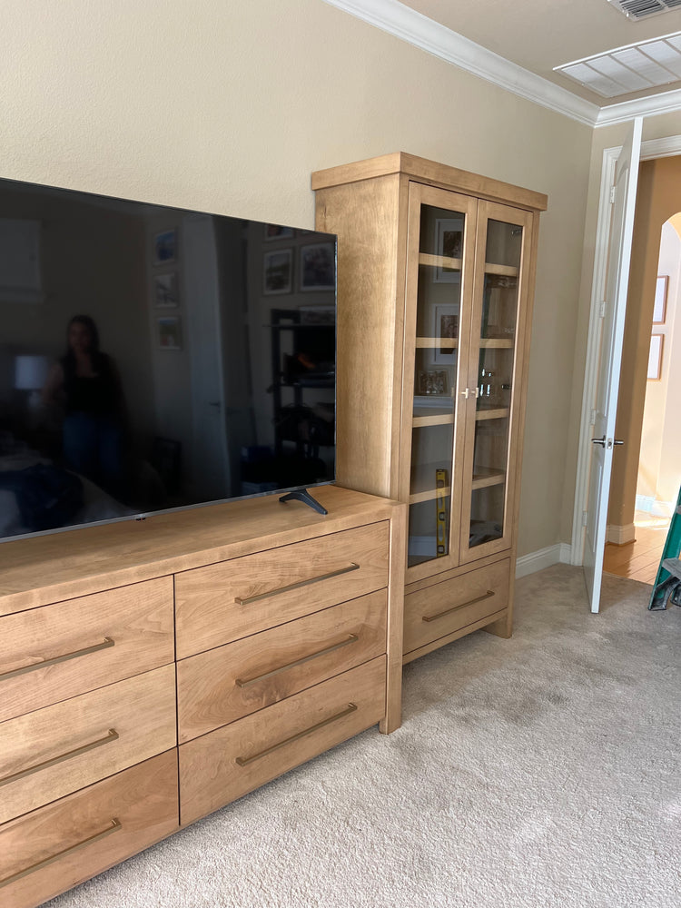 Wooden cabinet with glass doors and dresser in a bedroom.
